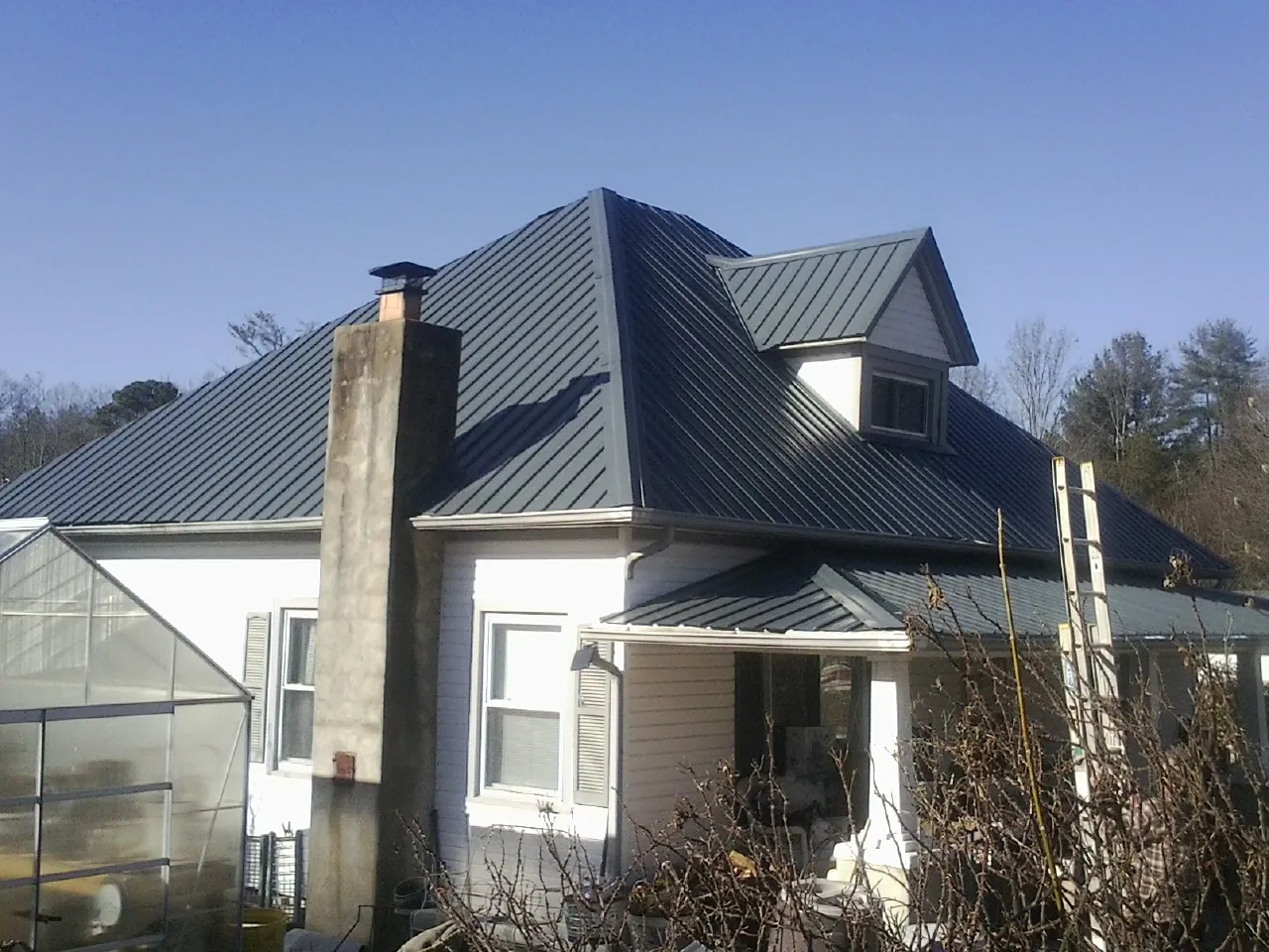 Dark blue standing seam metal roof on a white farmhouse with dormer — Slate & Tile Roof Repair by Roofing Brothers in Counce
