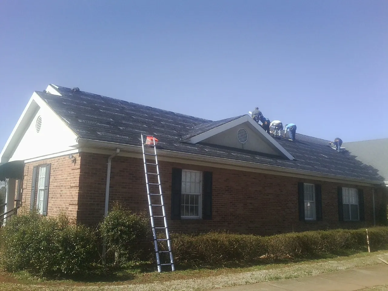 Crew tearing shingles off a brick ranch roof with a ladder set — Metal Roof Repair work by our crew in Counce