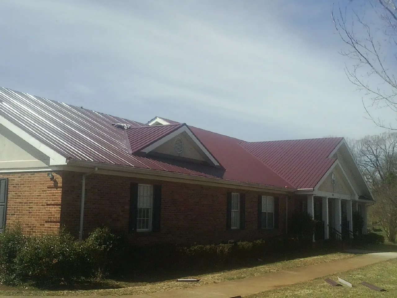 Red metal roof with gabled entries on a long brick building, from a Hail Damage Roof Repair job in Counce