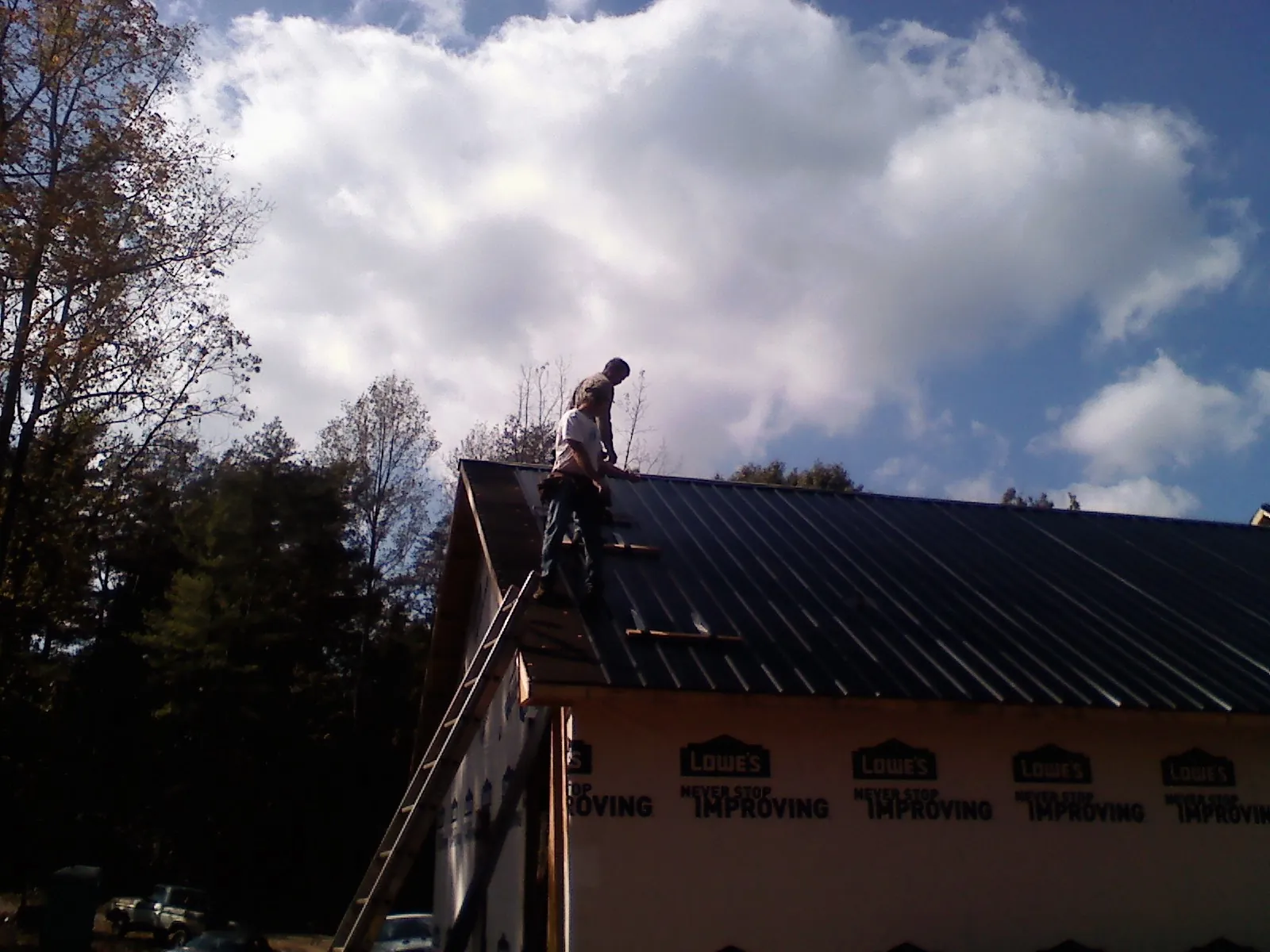 Roofer fastening dark metal panels high against a cloudy sky in Counce