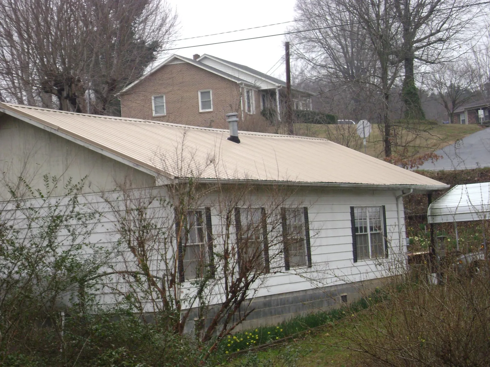 Tan metal roof on a white sided house set into a hillside — Commercial Roofing by Roofing Brothers in Counce